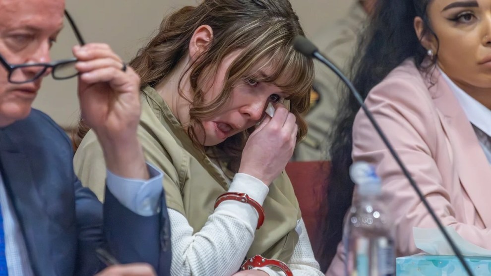 Hannah Gutierrez-Reed, a young woman wearing handcuffs and a prison uniform, wipes away tears while sitting in court with lawyers at her side.