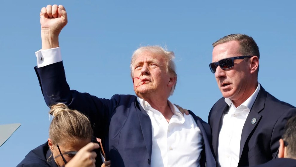 Donald Trump holds up his fist on stage with Secret Service around him.